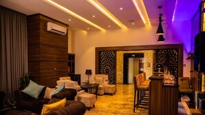 A modern lounge area with a sofa set, a small bar area, and a decorative wall. - OMEDEL LUXURY (Enugu)
