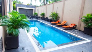 A swimming pool with lounge chairs and potted plants. - OMEDEL LUXURY (Enugu)