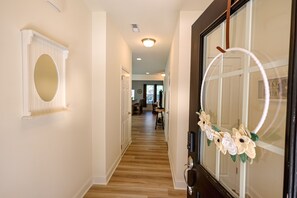Un couloir doté d’un plancher en bois, d’une porte blanche ornée d’un miroir et d’une couronne décorative.