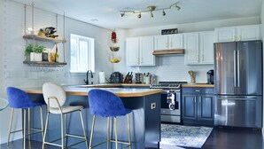 A modern kitchen with white cabinets, a stainless steel refrigerator, and a bar area with blue bar stools. - Bright & Spacious 3 Bedroom Home in Coveted Loveland Neighborhood! (Loveland)