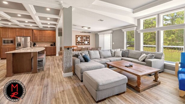 A spacious living area with a large L-shaped sectional sofa, a wooden coffee table, and a kitchen area with wooden cabinets and a built-in refrigerator.