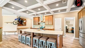A kitchen with a central island, bar stools, wooden cabinets, and a ceiling with recessed lighting.