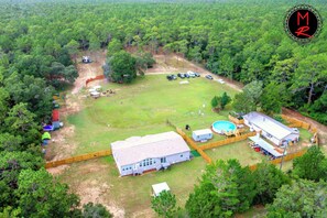 An aerial view of a property with a large grassy field, a swimming pool, a house, and several vehicles parked.