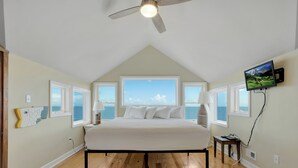 A bedroom with a large bed, a ceiling fan, and a TV mounted on the wall. - Island Rhythm: Beachfront, Community Pool, Hot Tub, Pet Friendly! (St. George Island)