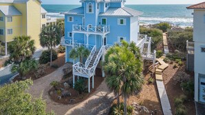 A multi-story coastal building with a blue exterior, white railings, and a staircase leading to a deck. - Island Rhythm: Beachfront, Community Pool, Hot Tub, Pet Friendly! (St. George Island)