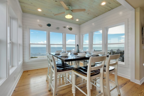 A dining area with a view of the ocean, wooden ceiling, and white walls.