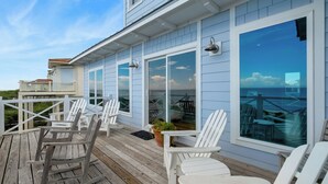 A wooden deck with white chairs and a rocking chair, overlooking a body of water. - Island Rhythm: Beachfront, Community Pool, Hot Tub, Pet Friendly! (St. George Island)