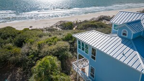 A coastal house with a metal roof, a deck, and a view of the beach and ocean. - Island Rhythm: Beachfront, Community Pool, Hot Tub, Pet Friendly! (St. George Island)