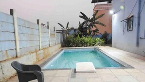 Una piscina petita a l'aire lliure amb una cadira de relaxació blanca i una altra negra.