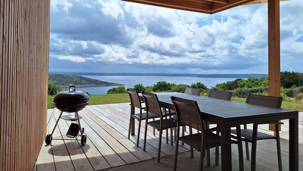 Eine Außenpatio mit Holztisch und Stühlen, einem Grill und einem schönen Blick auf einen See und Hügel.