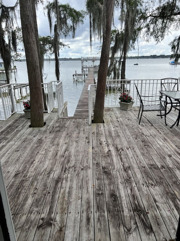 Un terrazzo in legno con ringhiera, piante in vaso e vista sull'acqua.
