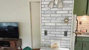 Una sala de estar moderna con televisor, sillas tapizadas en verde, una mesa blanca y una pared con diseño de ladrillo.