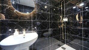 Ein Badezimmer mit einem weißen Waschbecken, einem Spiegel und einer Duschkabine mit goldener Duschbrause.