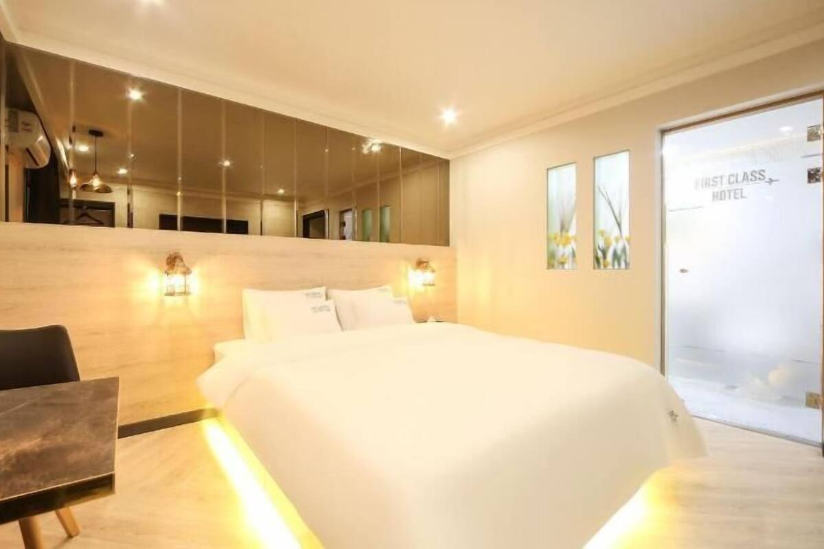 A modern hotel room with a large bed, bedside tables, a desk, and a mirror.