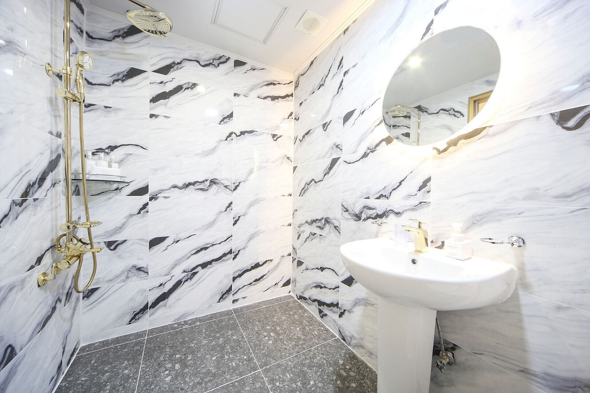 A bathroom with marble walls, a gold shower, and a white sink.