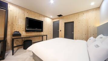 Een moderne hotelkamer met houten paneelwanden, een flatscreen televisie aan de muur, een bed met witte lakens, een klein bureau met stoel en een deur.