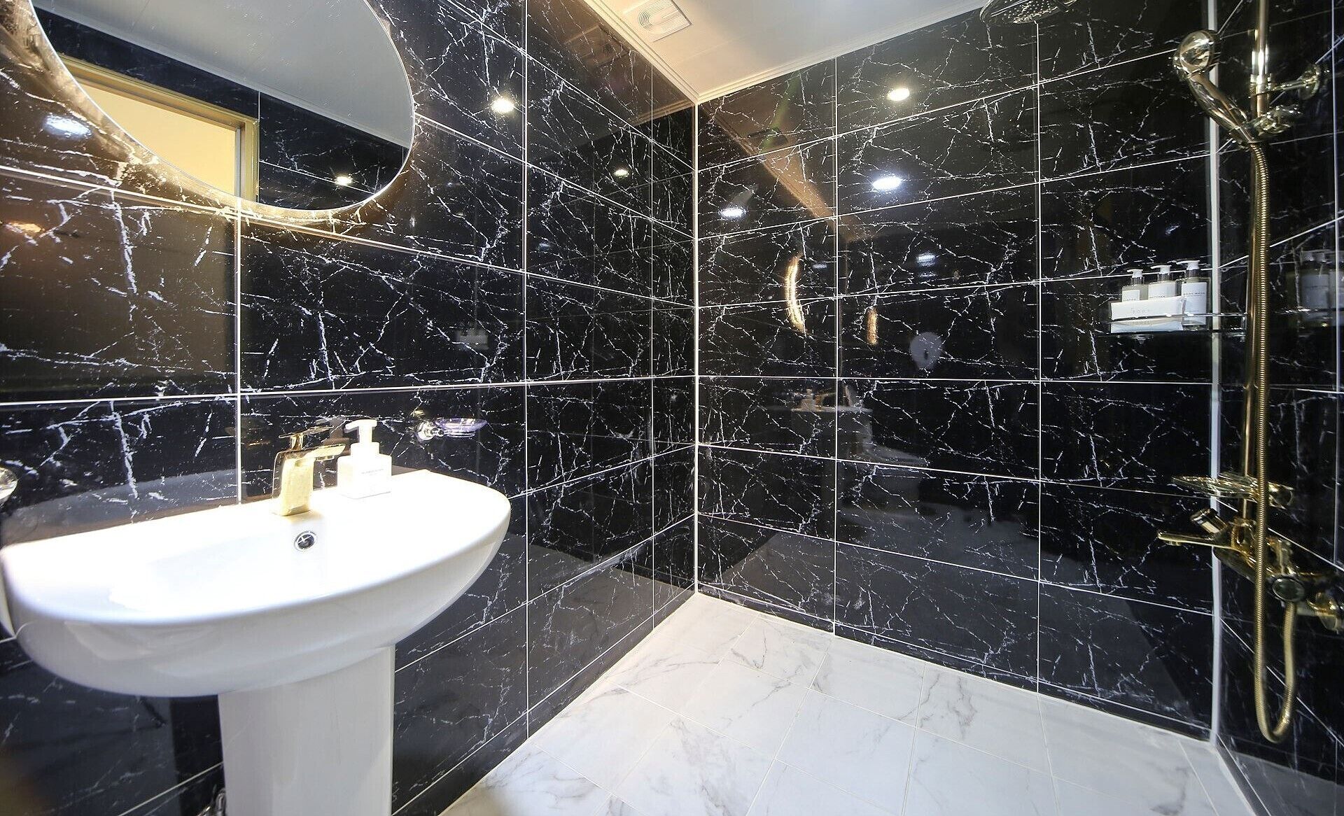 A bathroom with a white sink, black marble tiles, and a gold shower fixture.