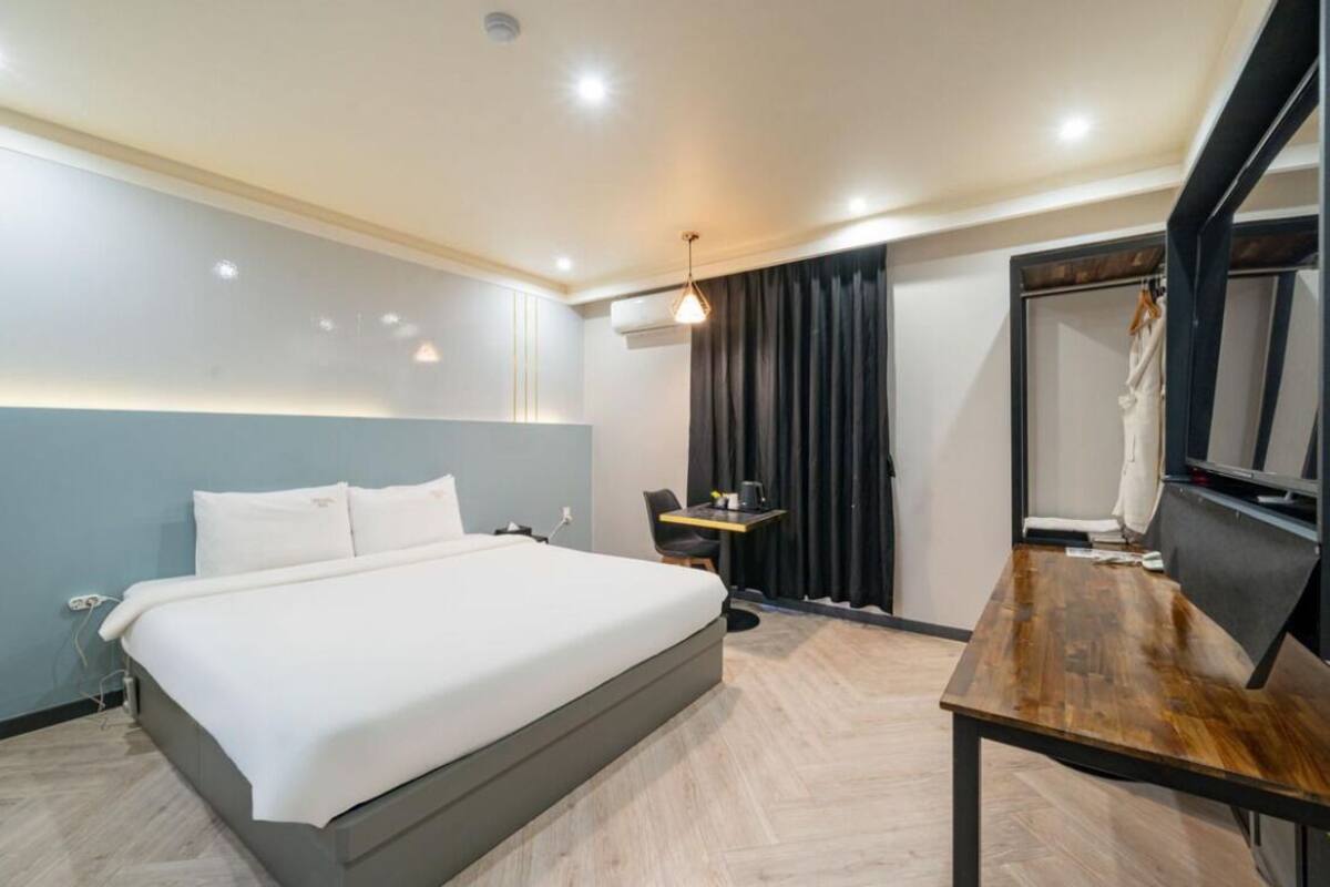 A modern hotel room with a large bed, a wooden table, a desk, and a mirror.