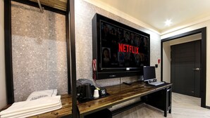 Ein modernes Hotelzimmer mit einem großen Flachbildfernseher an der Wand, einem Holztisch mit einem Laptop und einem Haartrockner auf der Ablagefläche.