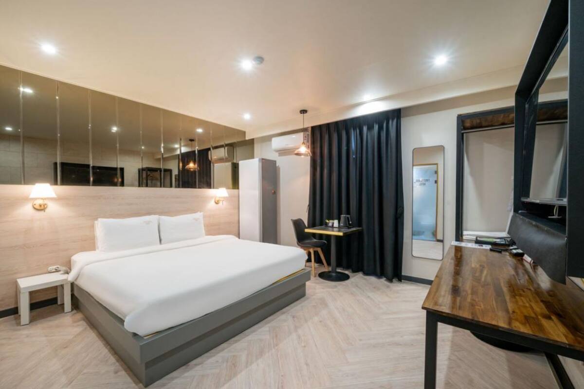 A modern hotel room with a large bed, a desk, a chair, a mirror, and a television.