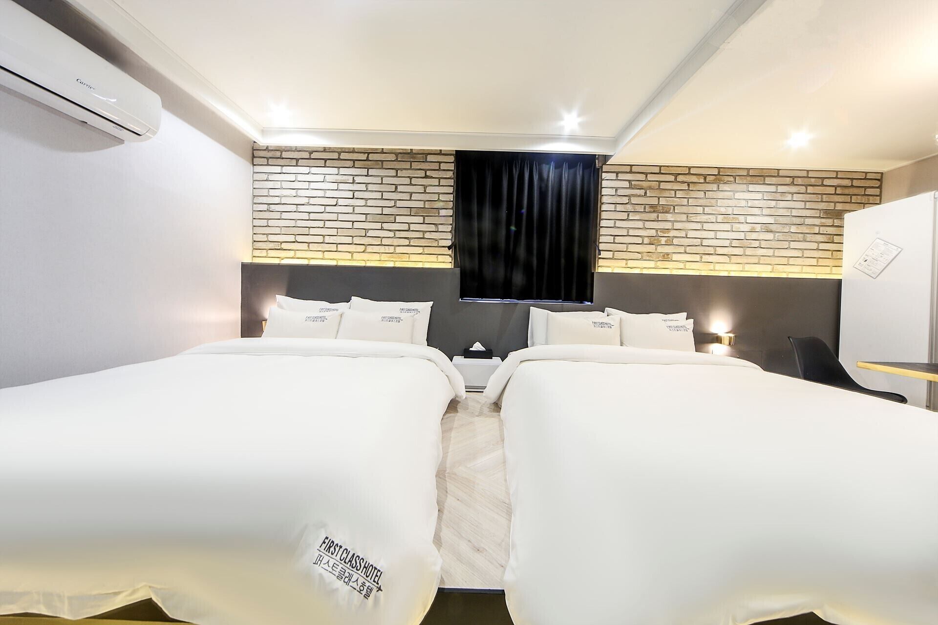 Camera d'albergo con due letti, una parete decorata in mattoni, una tenda nera e un condizionatore d'aria a muro.