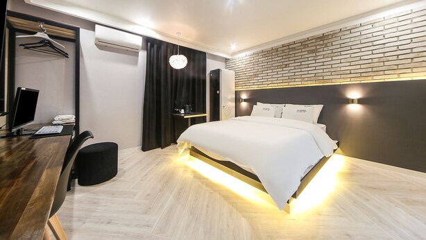 Ein modernes Hotelzimmer mit einem Bett, einem Schreibtisch mit Computer, einer Klimaanlage und einer Ziegelwand.