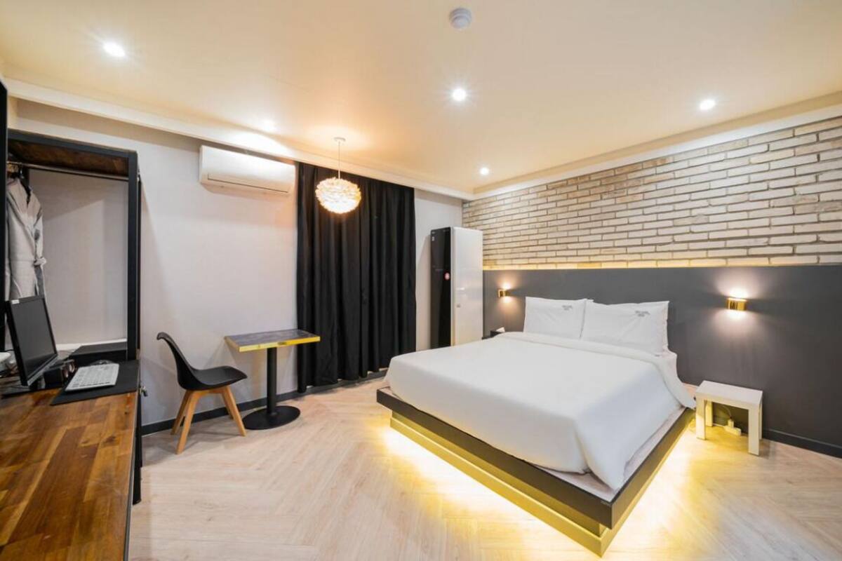 A modern hotel room with a large bed, a desk, a chair, and a small table.