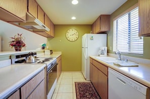 A compact kitchen with wooden cabinets, a stove, a refrigerator, and a clock on the wall.