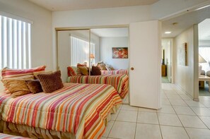 Un dormitorio con dos camas, un puertas corredera, un cuadro y un pasillo que conduce a otra habitación.
