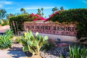 A sign for Palm Desert Resort Country Club with a cactus and desert plants in the foreground.
