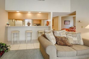 A modern living room with a sofa, a kitchen area with wooden cabinets, and a dining area with a table and chairs. - Desert Relaxation In-Between Two Fairways (Palm Desert)