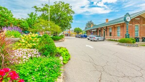 A street with a historic building, parked cars, and a variety of colorful flowers.