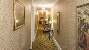 A narrow hallway with patterned wallpaper, a carpeted floor, and a chair in the foreground.