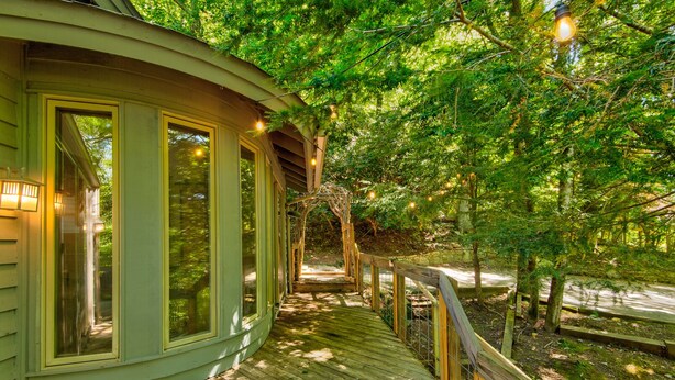 Eine Holzterrasse führt zu einem Haus mit großen Fenstern, umgeben von Bäumen.