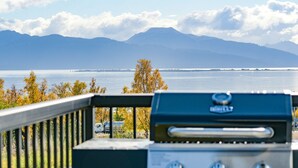 Ein Grill auf einem Balkon mit Blick auf ein Gewässer und Berge.