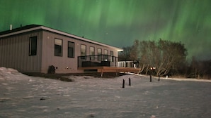 Ein modernes Gebäude mit Balkon, umgeben von Schnee, unter einem grünen Polarlicht.