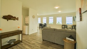 Ein modernes Wohnzimmer mit grauem Sofa, einem Holzesstisch und einer Küchenzeile inklusive Waschmaschine.