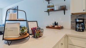 Una cocina con cafetera, estantes con plantas, dispensador de servilletas y un letrero de bienvenida.