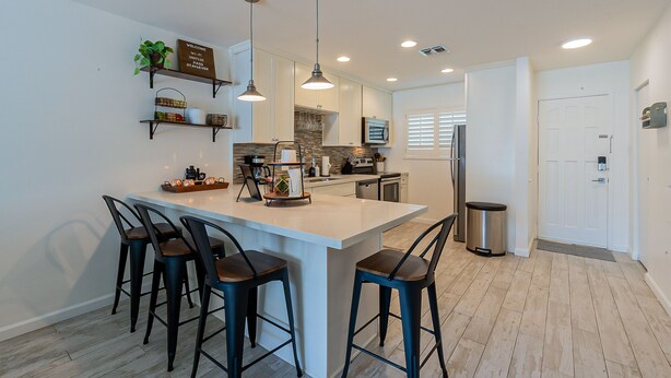 Una cocina moderna con una isla central, taburetes de bar, iluminación colgante y electrodomésticos integrados.