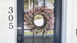 Une porte bleu foncé ornée d’une guirlande, avec le numéro de maison « 305 » et une lanterne fixée au mur.