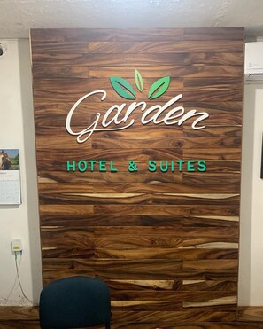 Puinen seinä, jossa on teksti ”Garden Hotel & Suites” ja logo, jossa on vihreitä lehtiä.