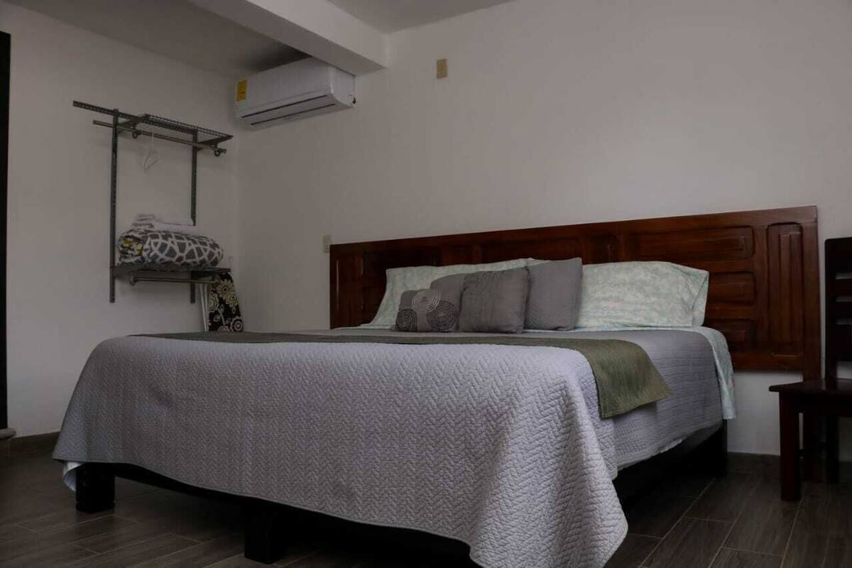 Ein Schlafzimmer mit einem Bett, einem Holz-Kopfteil, einer Wand-Klimaanlage und einem Regal mit einer gemusterten Decke.