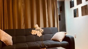 A modern living room with a dark sofa, a glass coffee table, and a vase with white flowers. - Hotel Garden Suites Tonlá (Tonalá)