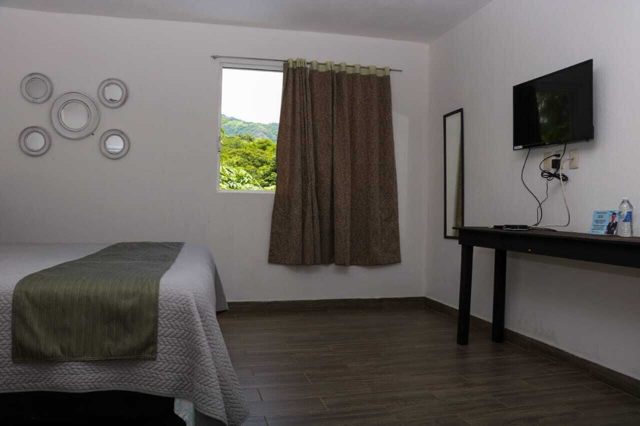 Una habitación con cama, ventana con cortinas, televisor de pantalla plana y una mesa con una botella y vasos.