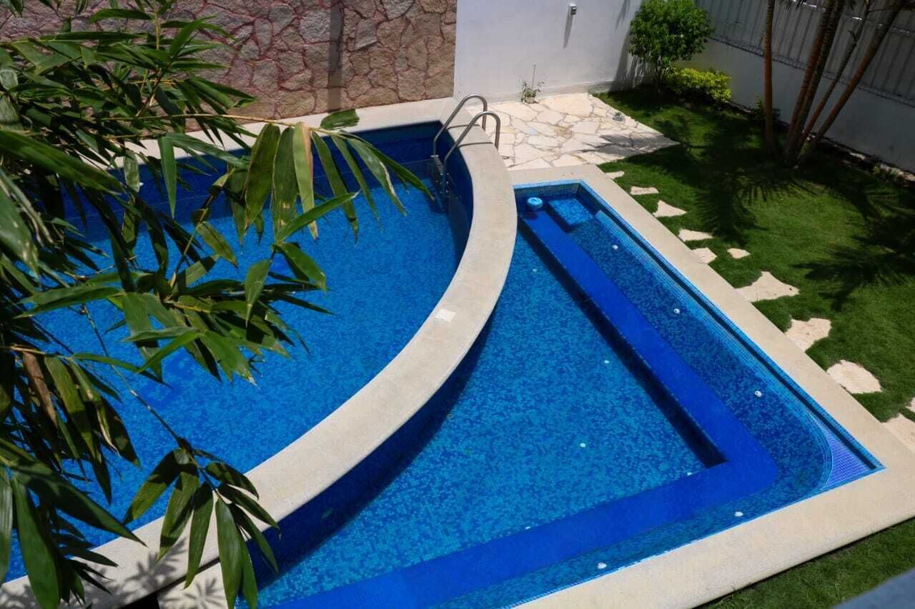 A curved swimming pool with a clear blue water feature, surrounded by a stone wall and a small patch of artificial grass.