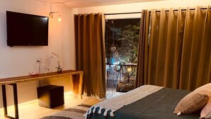 A modern bedroom with a bed, bedside table, TV, and a view of the outdoors. - Hotel Garden Suites Tonlá (Tonalá)