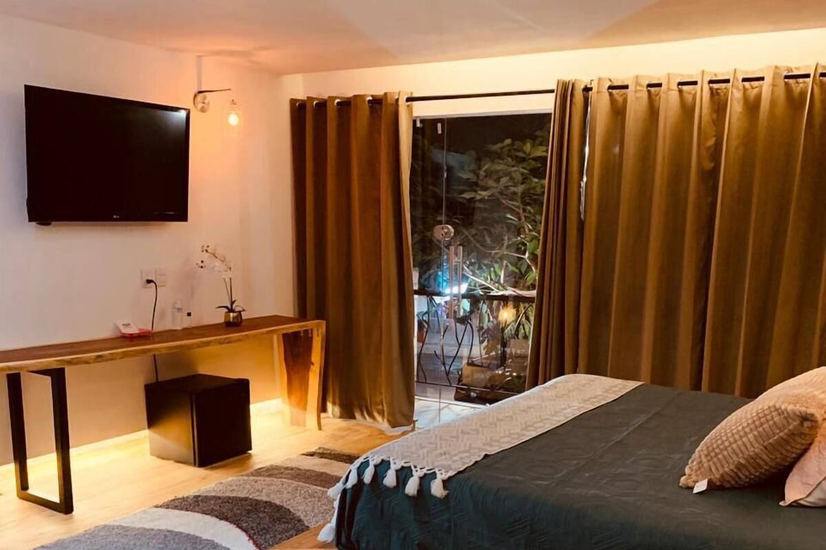 Ein modernes Schlafzimmer mit Bett, Nachttisch, Fernseher und Blick ins Freie.