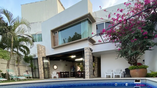 A modern pool area with clear blue water, stone pillars, and a covered seating area with chairs. - Hotel Garden Suites Tonlá (Tonalá)