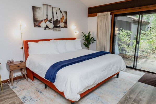 Een moderne slaapkamer met een groot bed, een nachtkastje met een lamp en uitzicht op de buitenlucht door een schuifdeur van glas.