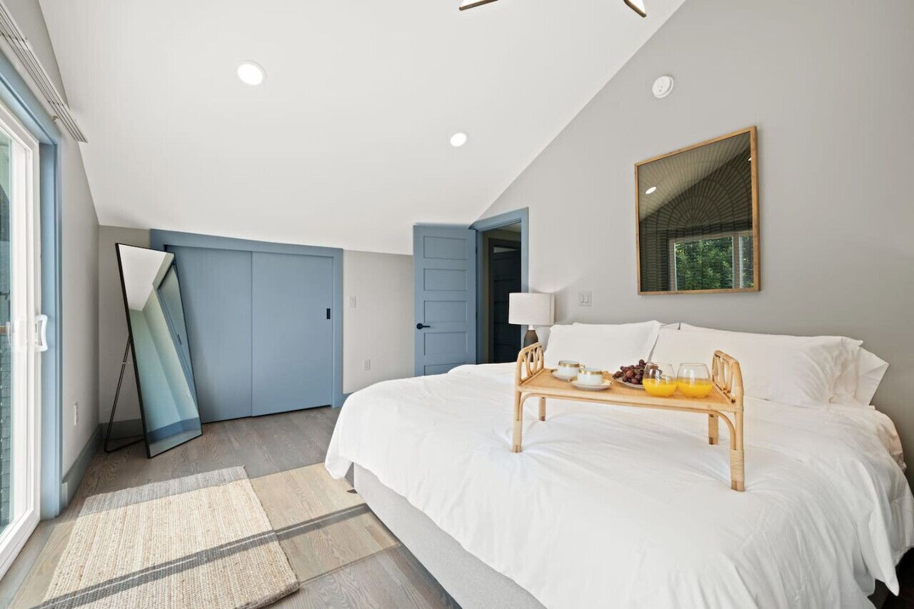 A bedroom with a large bed, a bedside table with a tray of fruit and juice, a mirror on the wall, and a view of the outdoors through a window.
